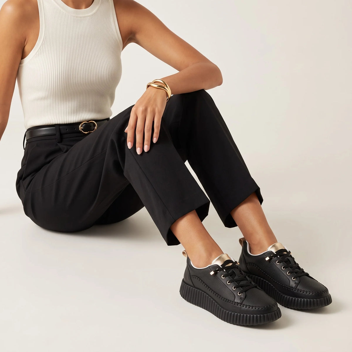 A black low-top platform sneaker with a textured upper, black laces, gold-tone eyelets, a white interior lining, and a chunky ridged sole