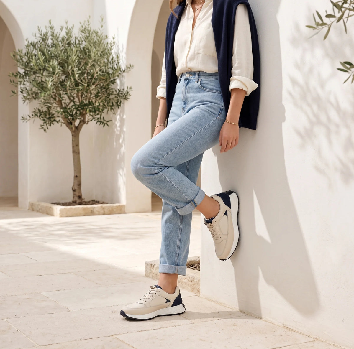 A low-top sneaker in light beige leather with a dark navy heel panel and a thick white midsole
