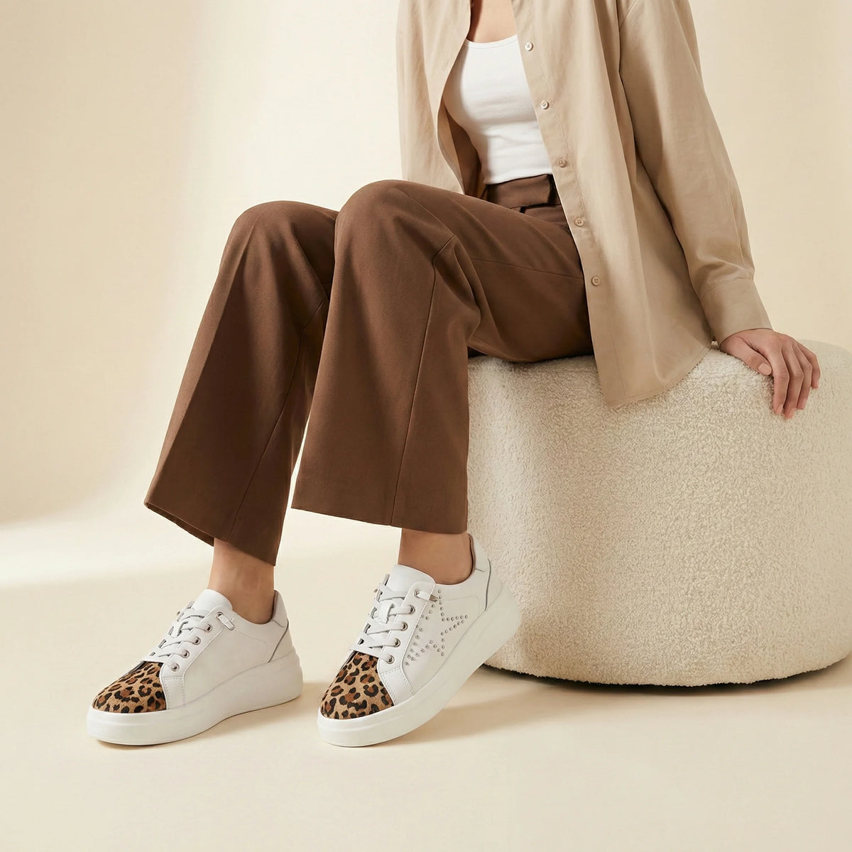 A white low-top platform sneaker with a leopard print toe cap and silver stud detailing on the side