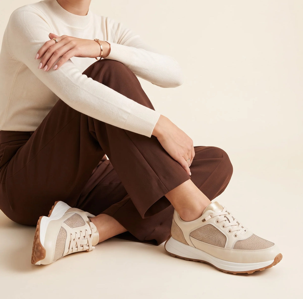 A low-top sneaker in beige and off-white with textured mesh panels, a thick white midsole, and a brown gum outsole