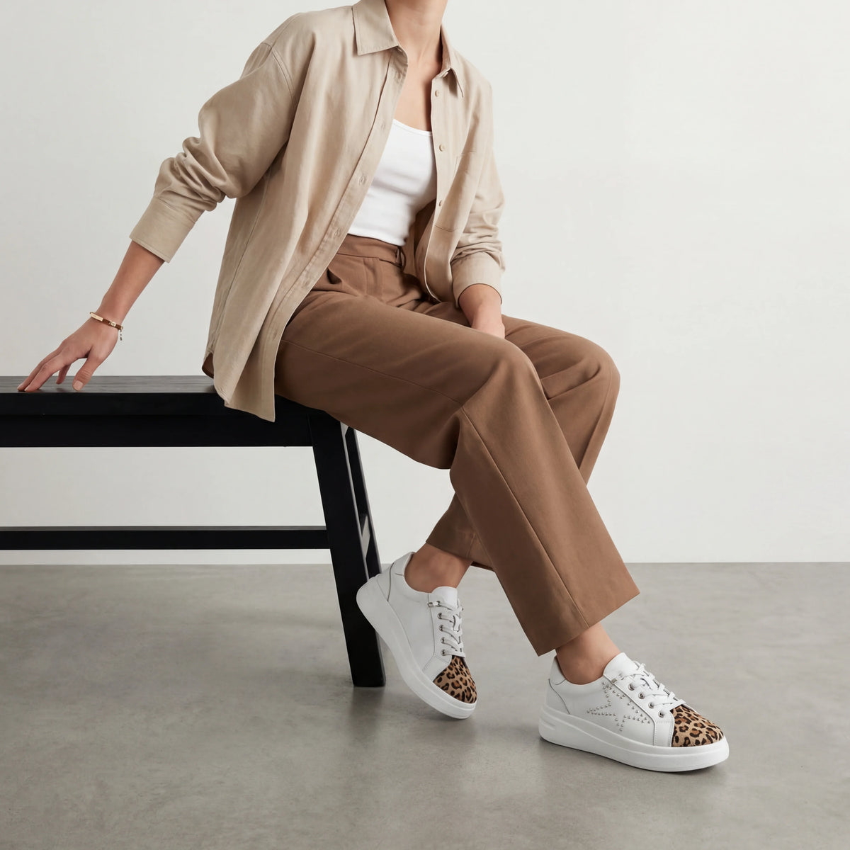 A white low-top platform sneaker with a leopard print toe cap and silver stud detailing on the side