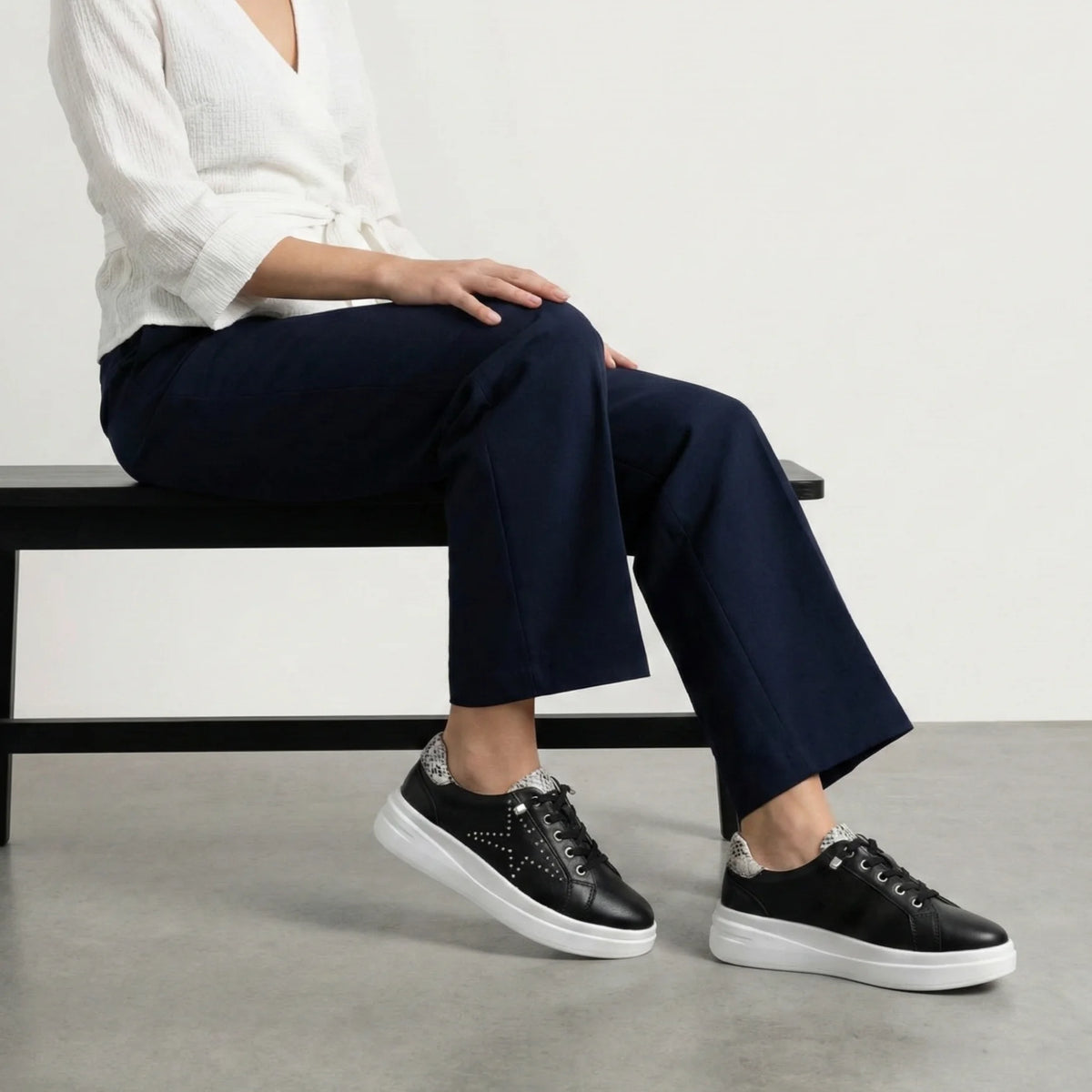 A black low-top platform sneaker with silver stud embellishments, a white platform sole, and a snakeskin-patterned heel tab