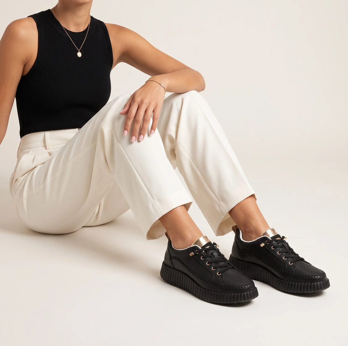 A black low-top platform sneaker with a textured upper, black laces, gold-tone eyelets, a white interior lining, and a chunky ridged sole