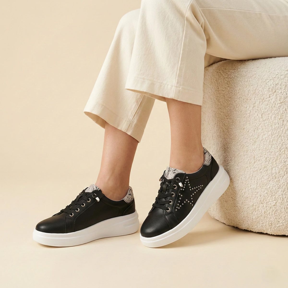 A black low-top platform sneaker with silver stud embellishments, a white platform sole, and a snakeskin-patterned heel tab